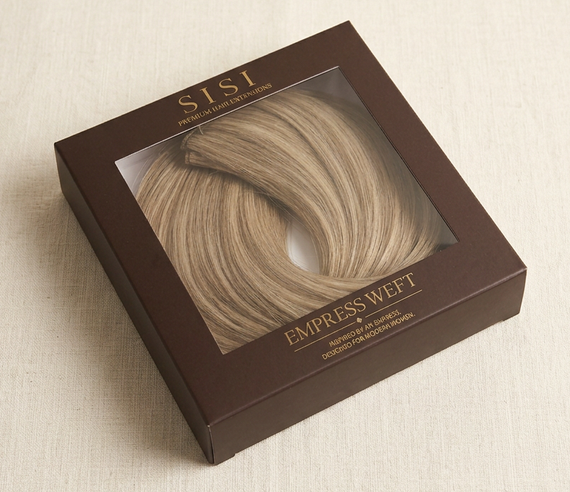 Studio photograph of the SISI Empress Weft packaging — espresso box with the weft visible through the window