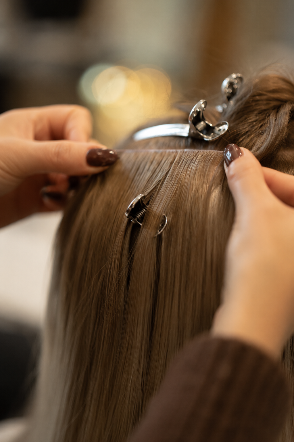 Close-up of a stylist installing a SISI Genius Weft — precision sectioning, clips and thread in a warm salon environment